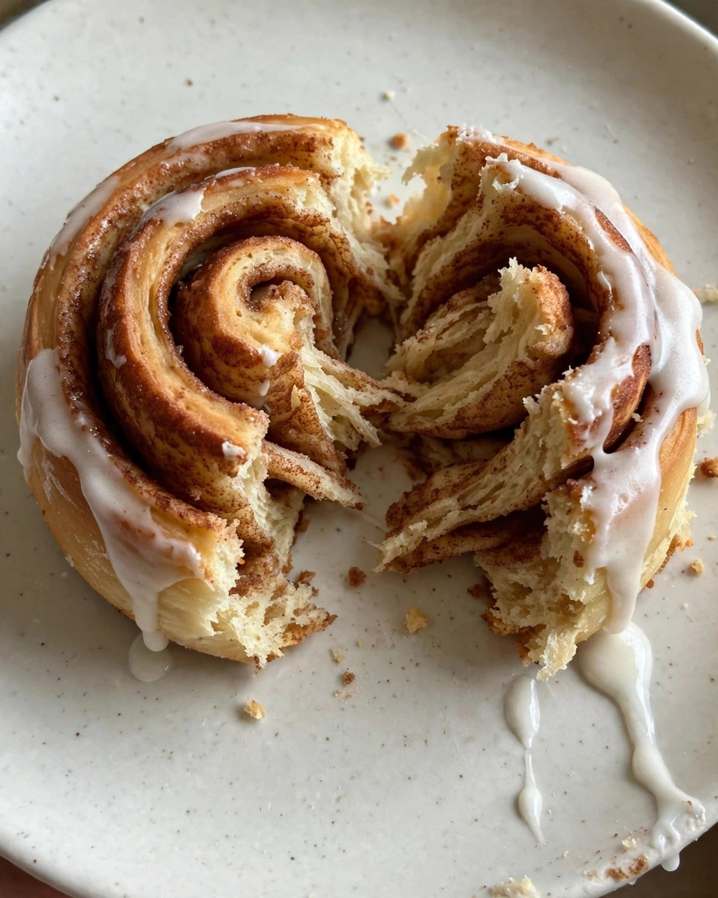 A warm cinnamon roll on a plate with icing dripping down the swirl