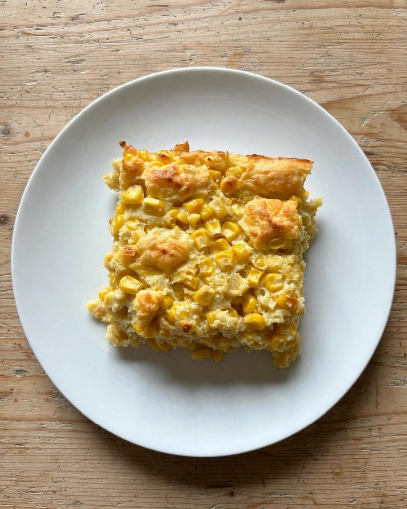 A square serving of corn casserole on a plain plate