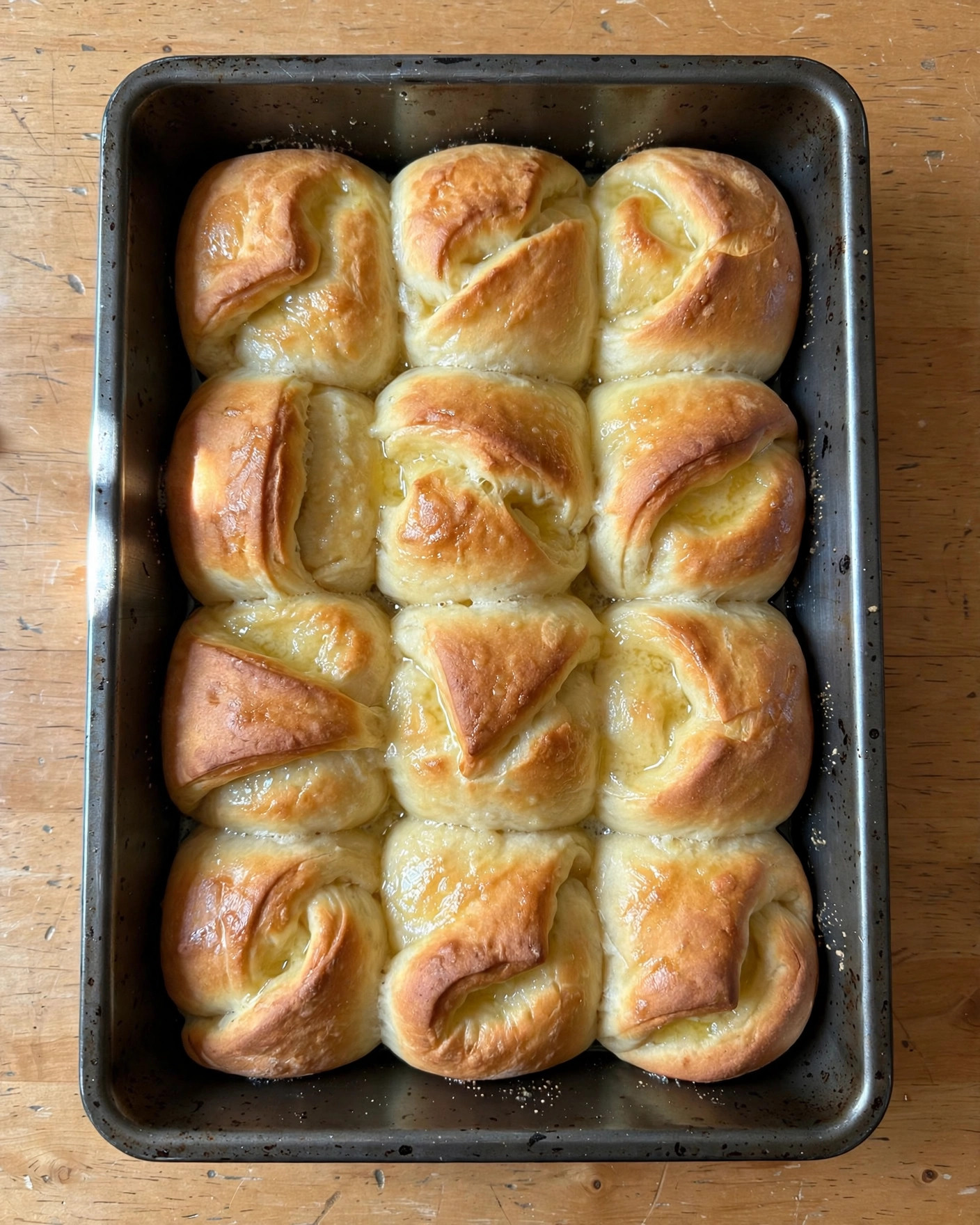 Golden Parker House rolls folded over in a baking pan, brushed with butter